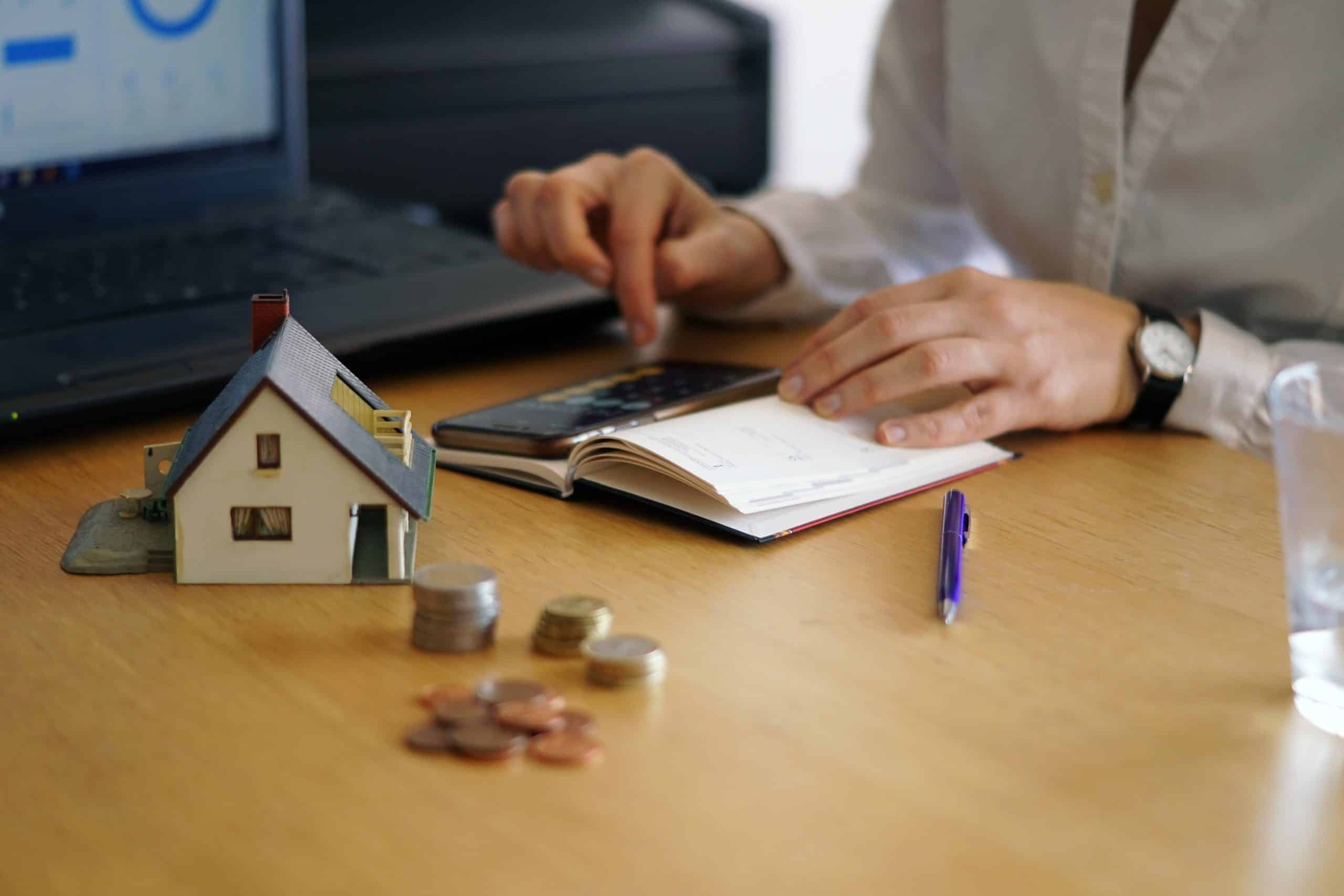 Affordable real estate financial planning with calculator, small house model, and coins on office desk for property investment.